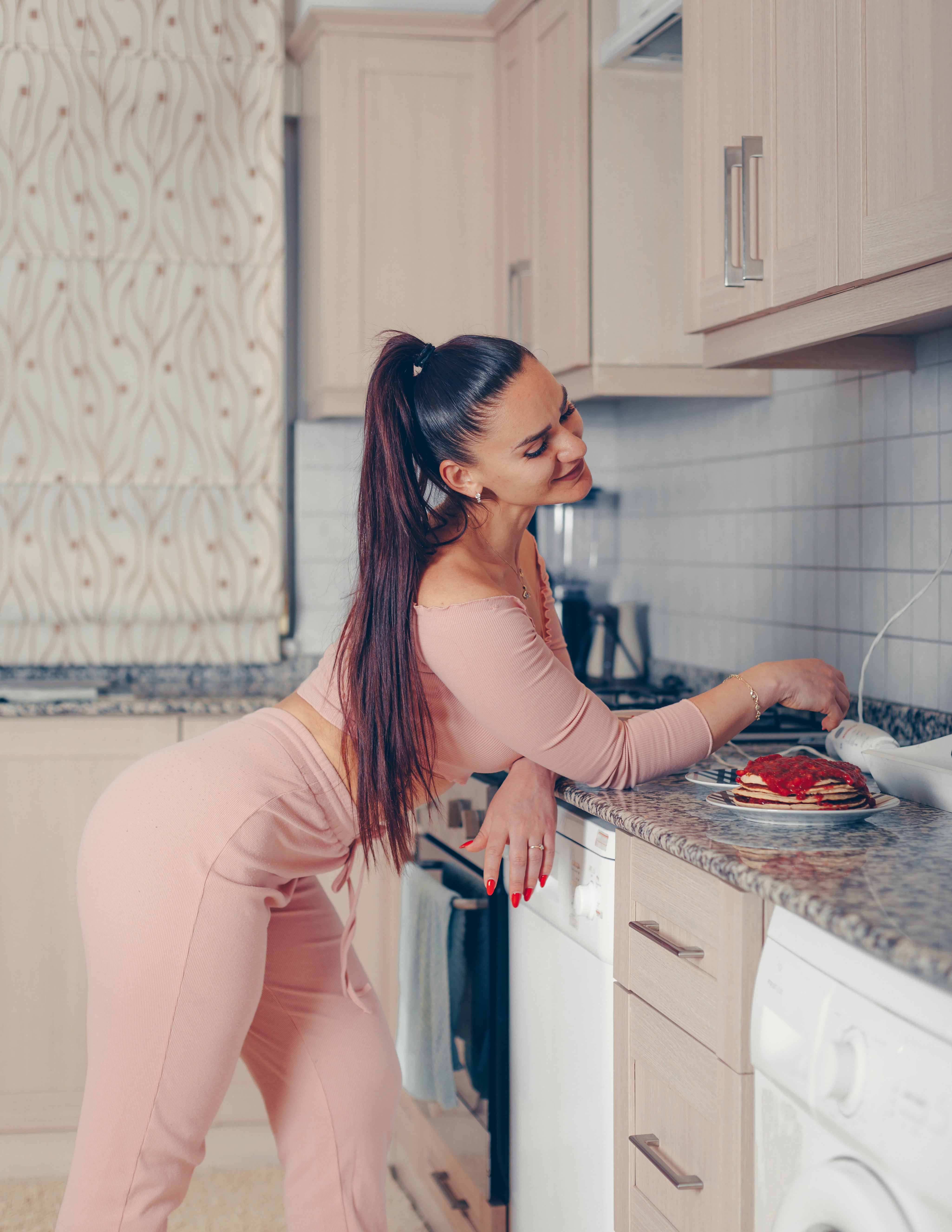 superbe-femme-debout-et-souriant-dans-la-cuisine-en-rose-et-saumon-crop-top-et-pantalon.jpg